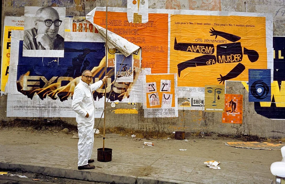 Saul Bass posant devant ses affiches de films, notamment "Exodus" et "Anatomy of a Murder", montrant son style graphique distinctif.