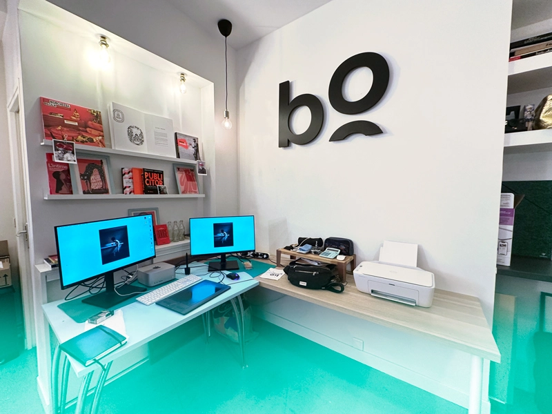 Bureau équipé avec deux écrans d'ordinateurs Mac et des livres design dans les locaux de bo école.