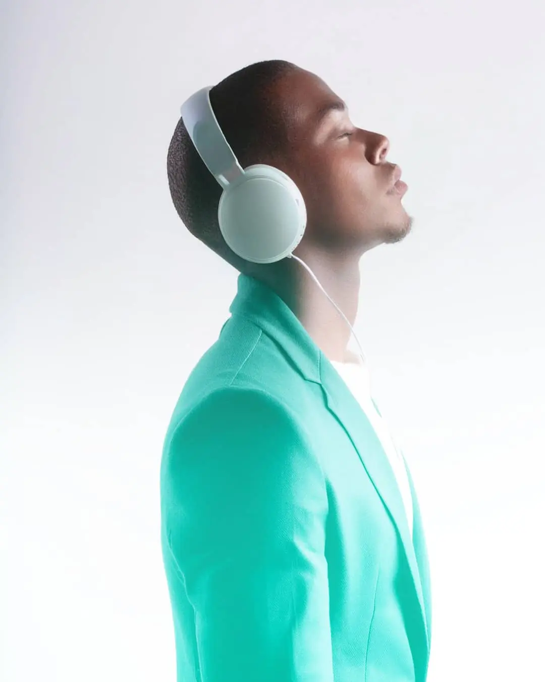 Étudiant portant un casque audio, habillé d'une veste verte, sur fond blanc, symbolisant créativité et immersion.