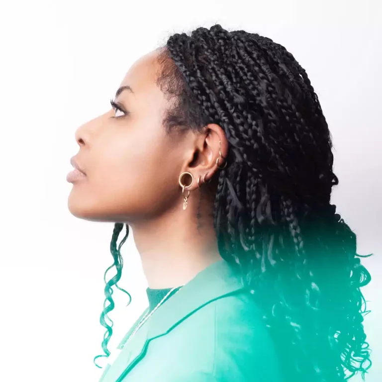 Portrait de profil d'une femme avec des cheveux tressés et des boucles d'oreilles, portant un blazer vert. Elle regarde vers la gauche, symbolisant le présent tourné vers l'avenir. Une légère teinte verte est ajoutée pour évoquer la créativité et la croissance, alignée avec une identité visuelle forte et cohérente.