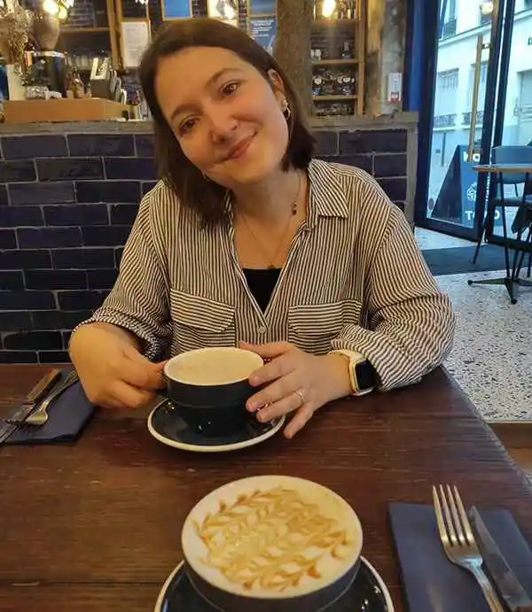 Thelma, ancienne professionnelle de santé reconvertie graphiste à distance chez bo école, souriante à une table de café